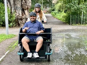 Ein Mann mit Fahrradhelm sitzt vorne in einer Fahrradrikscha. Eine Frau mit Helm fährt diese.