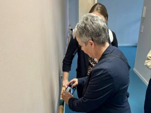 Eine Frau hält die Kamera ihres Handys an einen Handlauf. Darunter ist ein dunkles Zeichen, das ertastet werden kann.