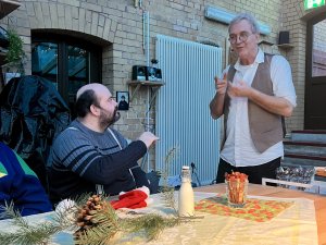 Ein Mann steht und gebärdet mit einem anderen Mann der an einem Tisch sitzt.