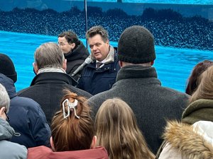 Ein Mann steht vor einem Mikrophon. Man sieht die K&ouml;pfe der Menschen, die ihm zuh&ouml;ren von hinten