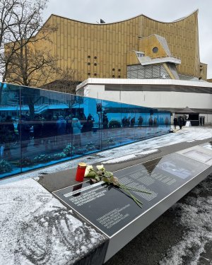 wei&szlig;e Rosen und ein Grablicht am Gedenk- und Informationsort. Im Hintergrund das Geb&auml;ude der Philharmonie in Berlin