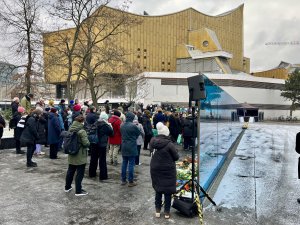 Viele Menschen stehen vor der blauen Wand am Gedenk- und Informationsort