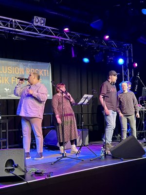 Vier Menschen stehen auf einer B&uuml;hne und singen in Mikrophone