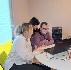 Drei Menschen gucken in den Bildschirm eines Laptops, der auf einem Tisch steht.