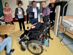Ein Mann sitzt im Rollstuhl, an dem ein Bildschirm befestigt ist. Mit ihm im Gespr&auml;ch ist der Bundesbehindertenbeauftragte, Herr Dusel und Herr Bell, Gesch&auml;ftsf&uuml;hrer von leben lernen