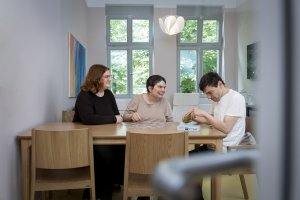 Drei Personen sitzen am Tisch und spielen ein Gesellschaftsspiel.